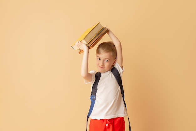 Cute smiling child with a backpack holding books in preparation for school on a beige background