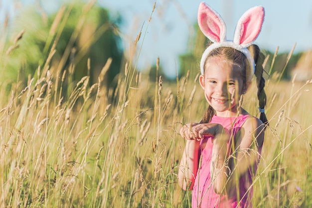 Cute smiling european girl with easter bunny ears in grass meadow outdoors