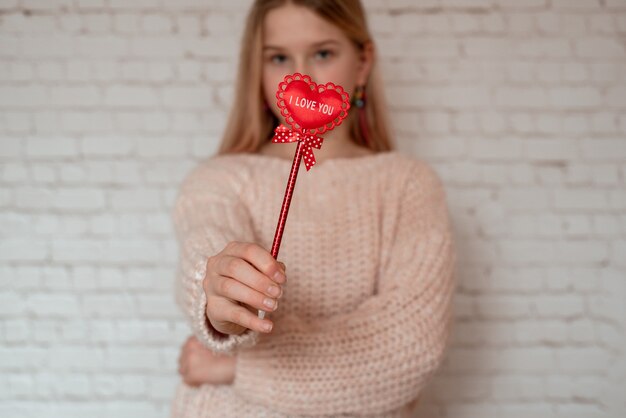 Cute smiling girl holding red fabric heart with I love you sign on stick