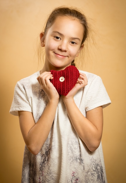 Foto carina ragazza sorridente che abbraccia il cuore a maglia rosso