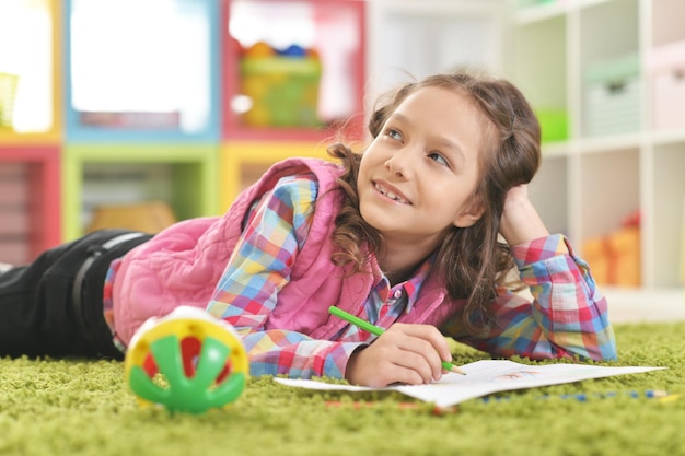 Cute smiling girl lying on floor and drawing at home