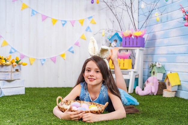 Cute smiling girl, lying on the grass with Easter eggs and looking into frame.