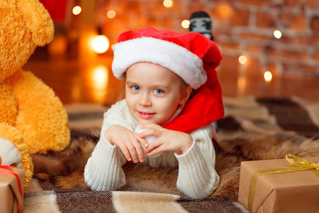 A cute smiling girl in a Santa hat against Christmas glitter