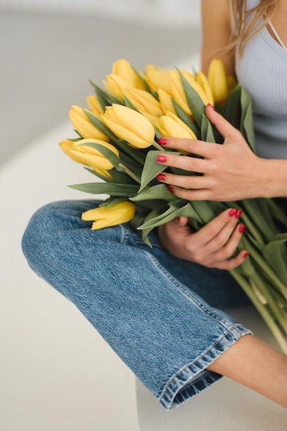 Cute smiling girl with a bouquet of yellow tulips in the interior