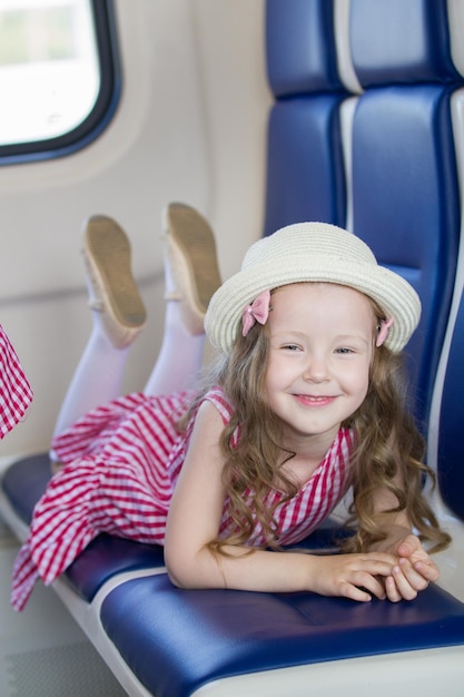 Cute smiling girl with long wavy hair in panama hat lying on armchair in the train