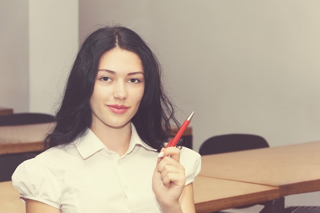 Ragazza carina sorridente con la penna, seduto in aula.