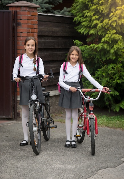 Carine ragazze sorridenti che vanno a scuola con le biciclette