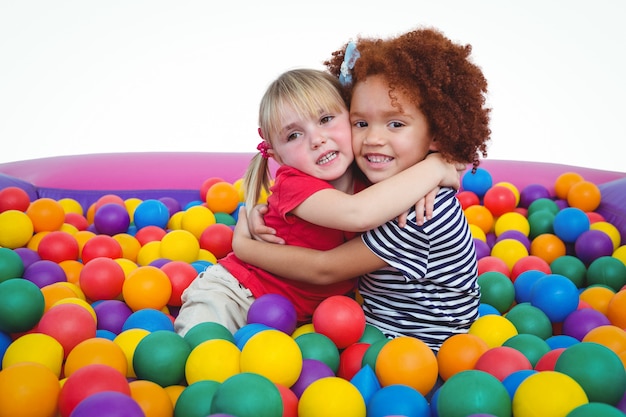 Cute smiling girls in sponge ball pool hugging