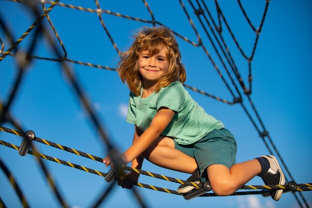 Милый улыбающийся ребенок лазит по сети на детской площадке веревочный парк, смешное лицо детей