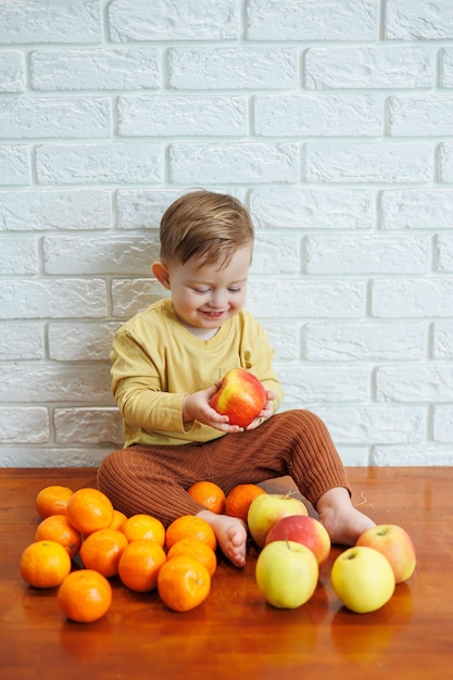 1つの新鮮なジューシーな赤いリンゴを食べるかわいい笑顔の子供。幼児のための健康的な果物