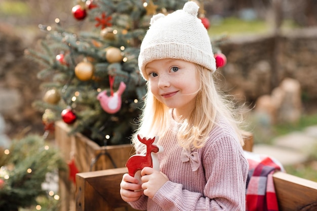 Cute smiling kid girl 4-5 year old wear knit hat and sweater decorating Christmas tree outdoor