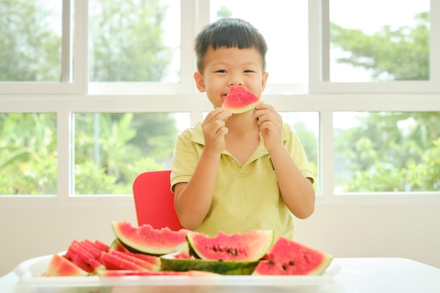 写真 夏にスイカを食べるかわいい笑顔の小さなアジアの学校の男の子の子供