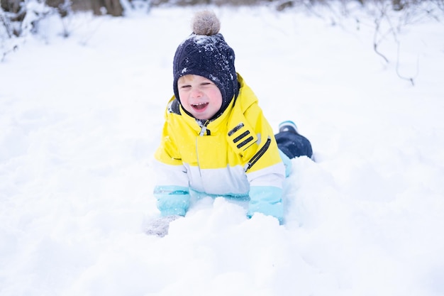 Cute smiling little boy with shovel playing with snow outdoors in winter forest