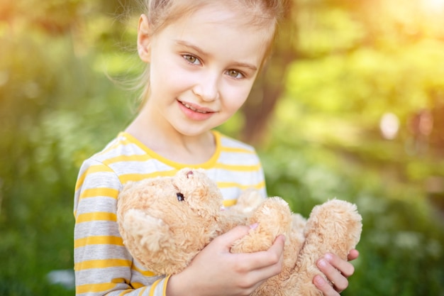 夏の公園で彼女のお気に入りのテディベアのおもちゃでかわいい笑顔の小さな子供の女の子