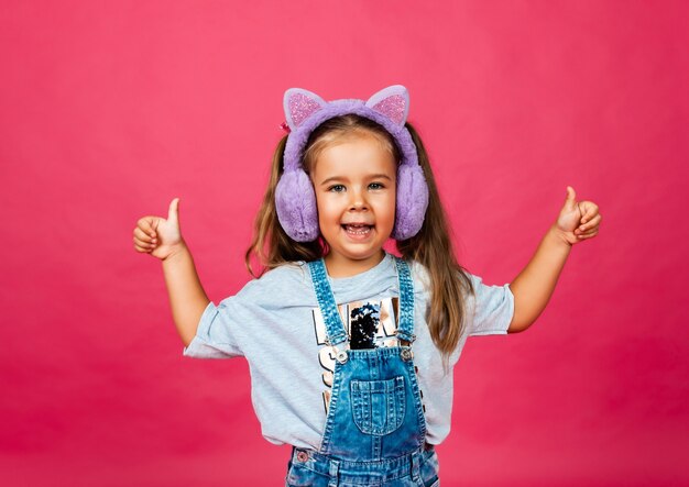 Cute smiling little girl having fun in fur headphones on a pink background.