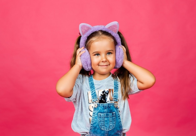 Cute smiling little girl having fun in fur headphones on a pink background.