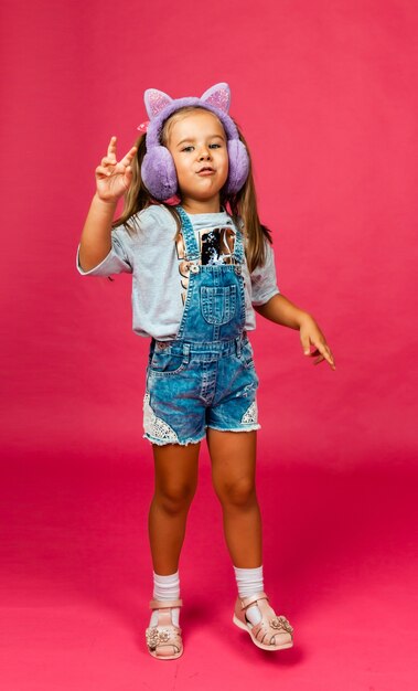 Cute smiling little girl having fun in fur headphones on a pink background.