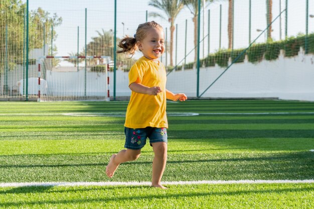 写真 緑のスポーツフィールドを走る可愛い笑顔の小さな女の子