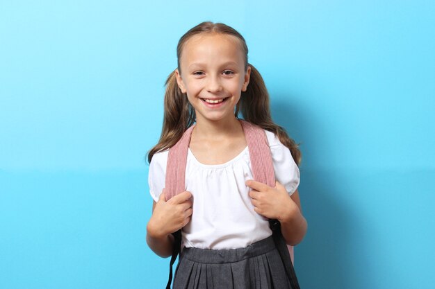 Cute smiling schoolgirl with a school backpack on a colored background