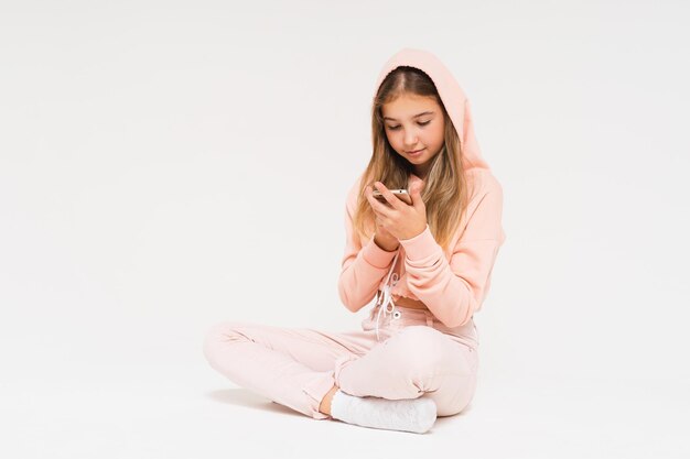 Cute smiling teen girl in pink hoodie using smartphone isolated on the white background