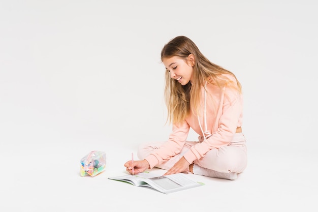 Photo cute smiling teen girl with long hair in pink hoodie doing homework isolated on the white background