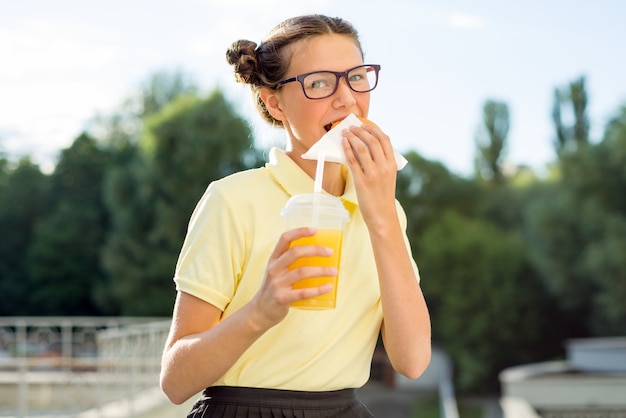 Cute smiling teenager holding a hamburger and orange juice.