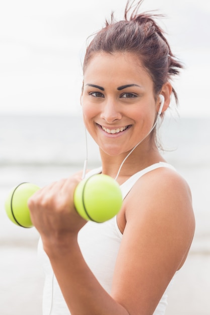 Cute smiling woman lifting dumbbells on the beach smiling at camera