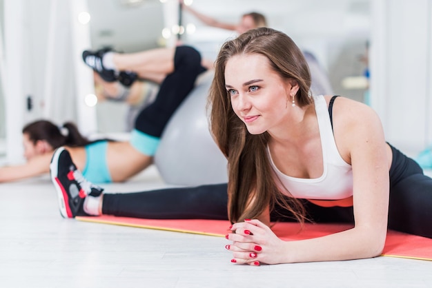 Giovane donna sorridente carina in abbigliamento sportivo che fa esercizio avanzato di divisione centrale piegandosi appoggiandosi sulle braccia in palestra