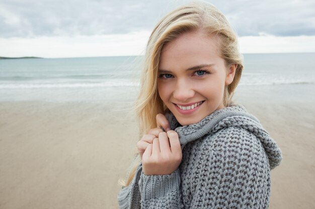 Cute smiling young woman in gray knitted jacket on beach