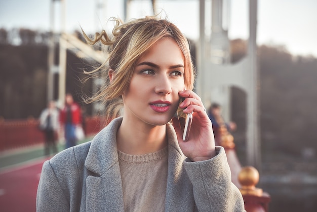 Cute smiling young woman talking on phone standing on the bride. Close up portrait