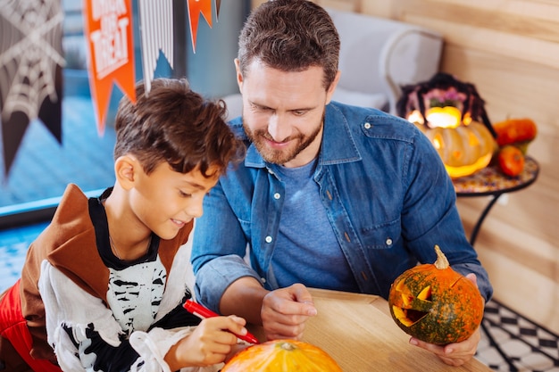 Figlio carino. vista dall'alto di raggiante figlio carino e padre amorevole che colorano le zucche per la celebrazione della famiglia di halloween