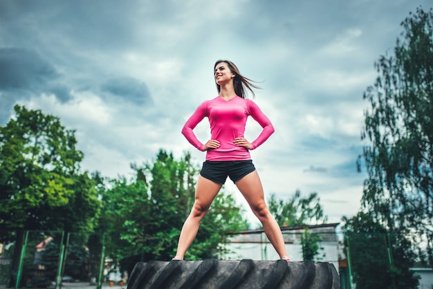 Cute sporty girl standing on huge tire outdoor