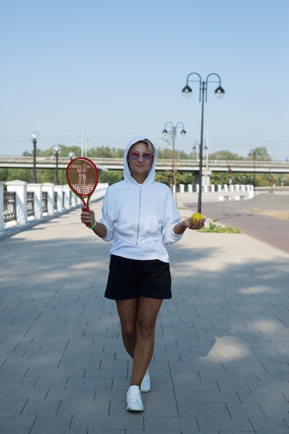 A cute sporty woman is holding racket and ball outdoor