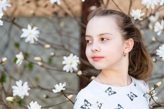 花のマグノリアの木の下でかわいい春のファッションの女の子