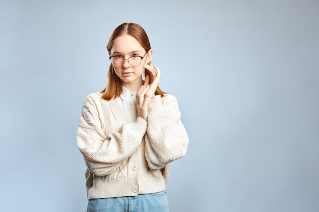 Cute student girl wearing beige sweater and stylish eyeglasses smiling, having rest after morning lectures at the college.