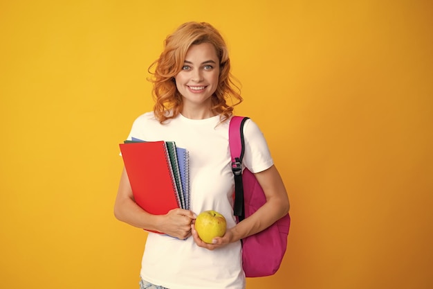 Cute student woman with backpack holds some documents and books over yellow background