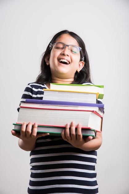 Piccola ragazza indiana o asiatica carina e studiosa che tiene o studia o legge un libro mentre si trova in piedi isolato su sfondo bianco