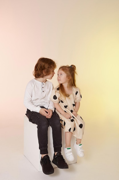 Cute stylish children on studio background two beautiful teens girl and boy sitting together stylish...