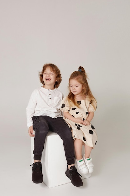 Foto bambini carini ed eleganti su sfondo studio due bei ragazzi ragazza e ragazzo seduti insieme alla moda...