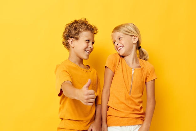 노란색 티셔츠를 입은 귀엽고 세련된 아이들은 어린 시절의 감정을 배경으로 나란히 서 있습니다.