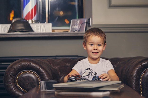 Cute stylish little boy at the barbershop in waiting room waiting for master. He plays with a toy chopper