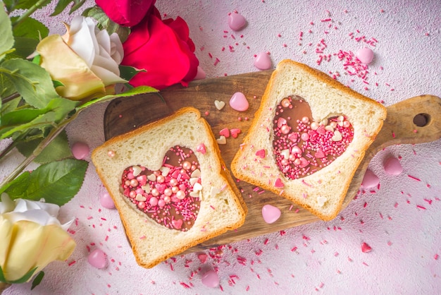 Cute sweet breakfast sandwich. Creative idea for Valentine day snack or lunch. Toast sandwich with peanut butter and chocolate pasta, with Valentine hearts red and pink sugar sprinkles top view.