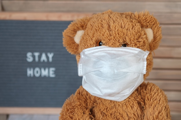 Cute Teddy bear in a medical mask on a gray felt Board with the text stay home. concept of home quarantine during the covid-19 coronavirus pandemic