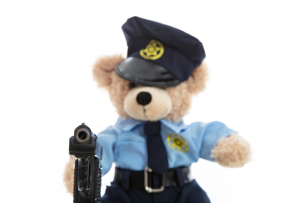 白い背景に対して隔離される銃を保持している警官の制服を着たかわいいテディ