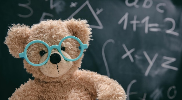 Симпатичный плюшевый мишка в очках и на черной доске с математикой