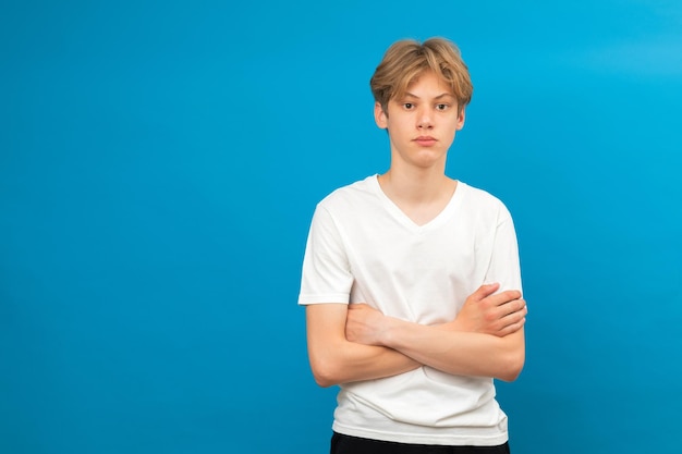 写真 青い背景で隔離のスタジオで腕を組んで立っている白いtシャツに身を包んだかわいい10代の少年