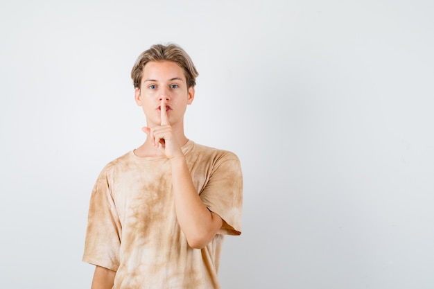 Cute teen boy showing silence gesture in t-shirt and looking serious , front view.