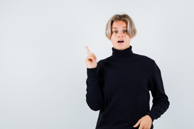 Cute teen boy in turtleneck sweater pointing up and looking smart