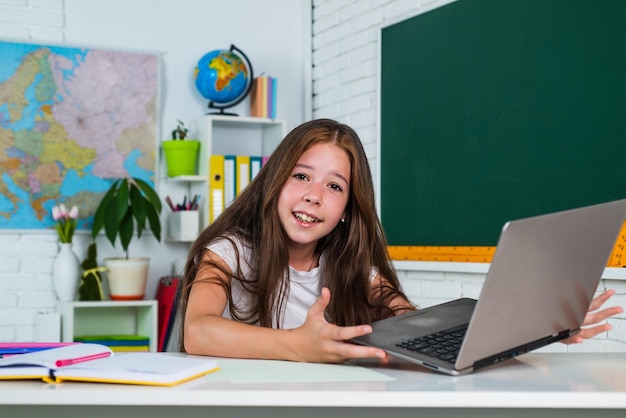 Cute teen child near chalkboard with laptop on online lesson back to school