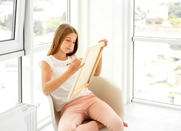 Cute teen girl drawing with pencil in the chair